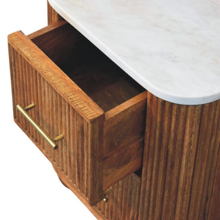 Detail view of the open wooden drawer, brass handle, reeded cabinet, and white marble top.