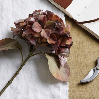 Close-up of the artificial hydrangea head showing variegated brown and mauve petals on white linen.