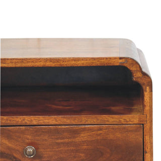 Detail of the chestnut bedside unit showing the curved top edge and the entrance to the open shelf.
