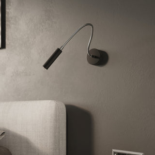 Black AXIL wall light mounted above the corner of a light grey fabric upholstered headboard.