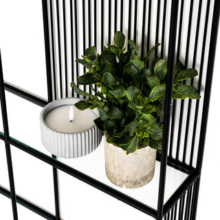 Detail shot of the clear glass shelf surface with a plant and candle against the vertical wire backing.