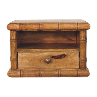 Amber oak finish bedside table with bamboo-style carved frame, open shelf, and one drawer with a metal knob. Plain studio shot.