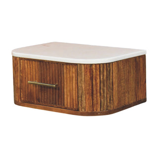 White marble surface resting on the curved, vertically fluted dark wood cabinet with brass drawer pull.