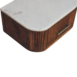 High-angle close-up showing the white marble surface, fluted dark wood body, and horizontal brass drawer handle.