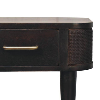 Dark wood bedside detail: brass handle, woven side panel, and tapered leg.