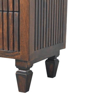 Detail of the dark wood nightstand's lower corner, showing the fluted side panel and turned feet.