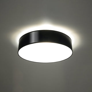 Black cylindrical ceiling light fixture illuminated, creating a soft light halo where it meets the ceiling.