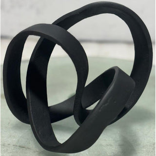 Close-up of the black cast knot ornament showing its looping shape and matte texture, resting on a light grey surface.