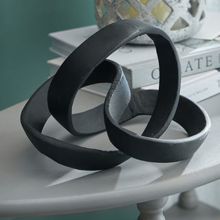 Cast knot sculpture resting on a painted side table, styled with books against a teal wall.