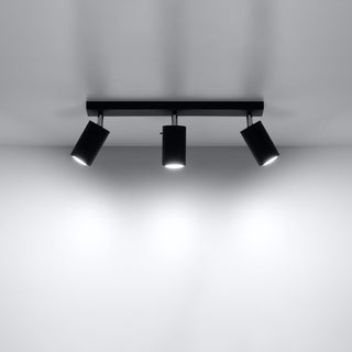 Black ceiling light with three spotlights shining bright light onto a white wall.