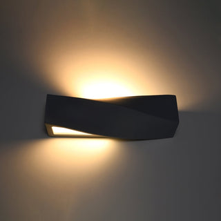 Black ceramic SIGMA wall light switched on, showing warm up and down illumination on a dark wall.