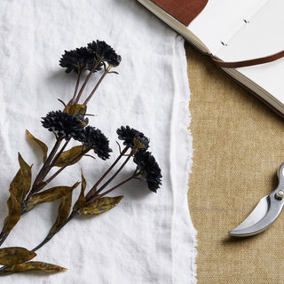 Close-up of black artificial chrysanthemum heads and stems lying across white linen and tan textured fabric.