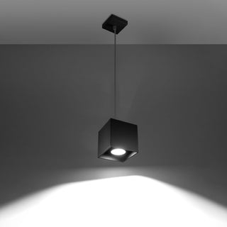 Black cubic pendant light fixture switched on, casting a bright downward spotlight beam.