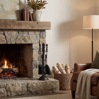 Black companion set on a rustic stone hearth next to a burning fire.