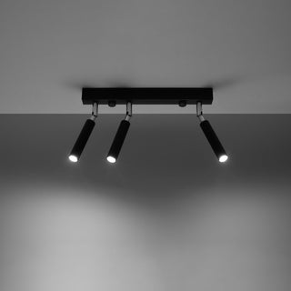 Black three-spotlight fixture illuminated, casting bright white light onto the dark wall below.