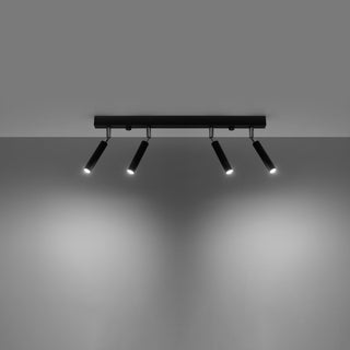 Black four-spotlight ceiling fixture illuminated, casting bright circular beams onto the grey wall below.