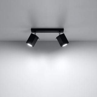 Black ceiling spotlight bar mounted on a white ceiling, casting two bright beams onto the wall.