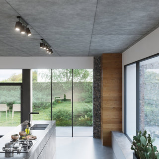 Pair of black track light fixtures mounted separately on a raw concrete ceiling in a contemporary kitchen.