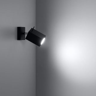 Black Merida spotlight mounted in a corner, casting a bright white beam onto the adjacent wall.