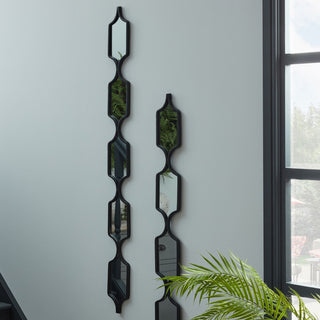 Two black metal mirrors displayed vertically side-by-side on a grey wall near a large window.