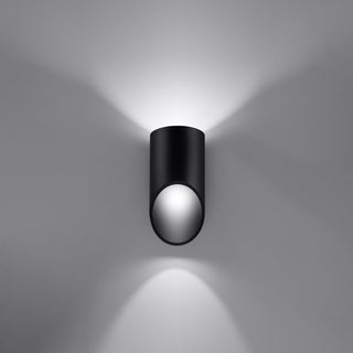 Black cylindrical wall lamp showing light projected upwards and downwards onto a pale wall.