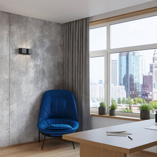 Black wall light mounted on a grey concrete wall in a contemporary office with a blue chair and city view.