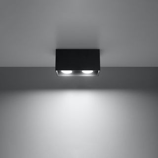 Black quad ceiling lamp illuminated, showing the concentrated downlight beam projected onto the wall.