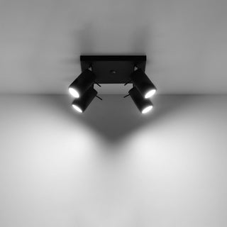 Black four-spot ceiling light illuminated, demonstrating the focused light beams onto the wall.