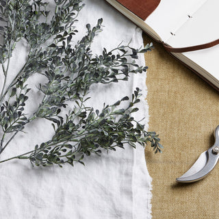 Close-up of the dark green artificial leaves and stems, showing the dusty texture against white linen.