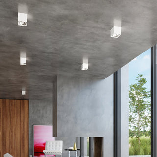 Five white square lamps mounted on a grey concrete ceiling in a minimalist room overlooking a garden.