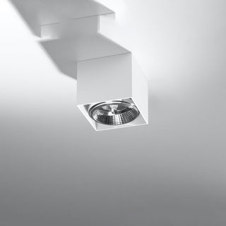 White square ceiling light fixture projecting from the ceiling, showing the chrome reflector and strong shadow detail.
