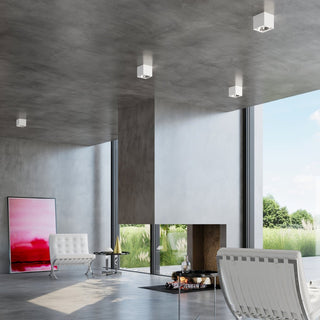 Four white square ceiling lamps installed on a concrete ceiling in a modern open-plan living space.