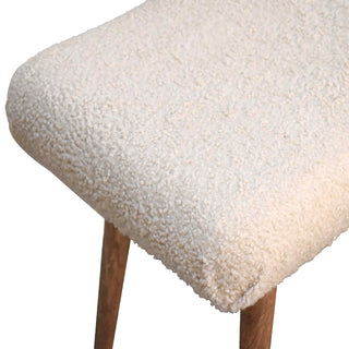 Close-up showing the fluffy cream boucle seat fabric meeting the angled wooden leg below.