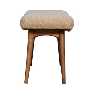 Low, front-on view of the cream boucle bench showing the arched wooden support structure between the angled legs.
