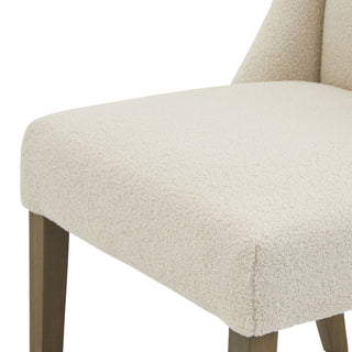 Close-up detail of the cream bouclé fabric seat surface and the front corner above the dark wood leg.