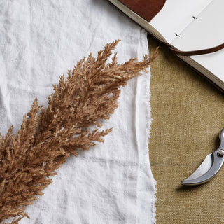 Detail shot showing the texture of the brown faux pampas grass against white linen and khaki fabric.