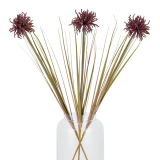 Three artificial burgundy aster stems with long green stalks arranged in a clear vase.