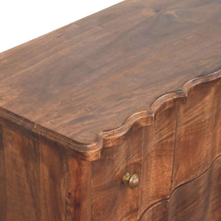 Close-up detail of the dark wood chest showing the rich grain, the serpentine top edge, and a brass knob.