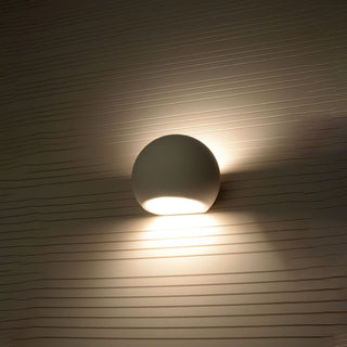 Ceramic wall light globe mounted on a textured wall, casting a warm light wash above and below the fixture.