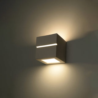 Close view of the cubic wall light showing three distinct areas of warm light on the grey wall.