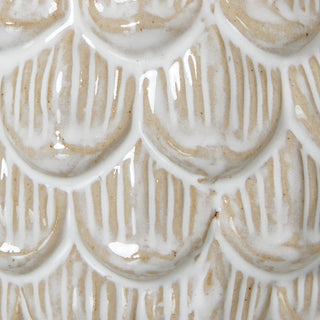 Macro detail of the ceramic pine cone texture. Glossy white glaze highlights the raised scales over a beige base.