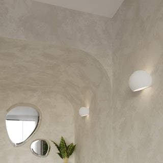 Two ceramic wall lights illuminating a textured beige hallway with an arched opening and decorative mirrors.