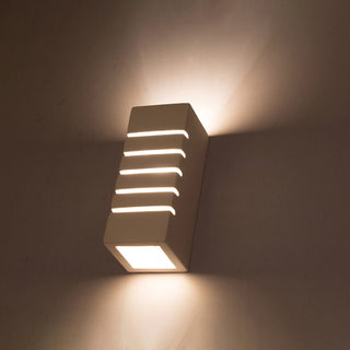 Ceramic wall lamp illuminated, showing light cast upwards, downwards, and through five horizontal slits.