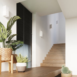 Three unlit ceramic wall lamps installed in a modern stairwell with wooden steps and potted plants.