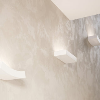 Close view of rectangular and curved ceramic wall lights illuminating a textured corner wall.