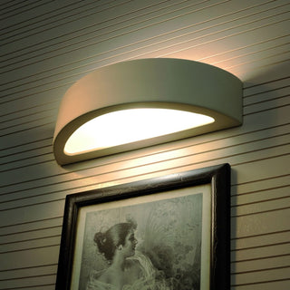 Wall light fixture illuminating a framed picture below it, mounted on horizontally striped wallpaper.