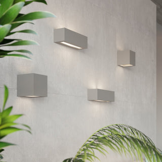 Four grey ceramic wall lights of varying shapes installed on a pale tiled wall, casting warm uplight and downlight.