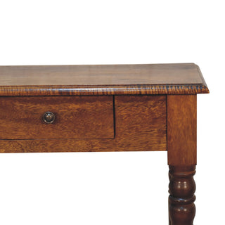 Close detail of the desk's chestnut wood grain, single drawer front, metal handle, and upper turned leg.