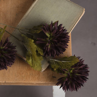 Close-up of three artificial chocolate chrysanthemum heads and green leaves on a closed sage book.