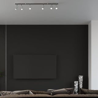 Styled room scene showing six adjustable chrome spotlights installed on the ceiling above a dark wall.